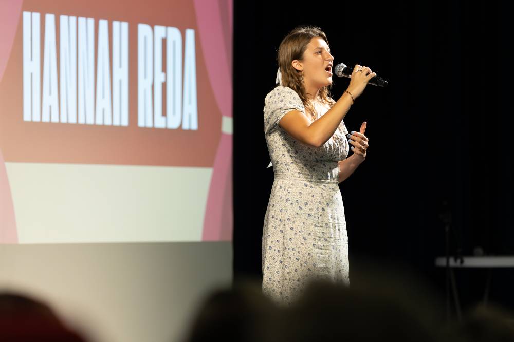 Hannah Reda singing on stage holding up a microphone.